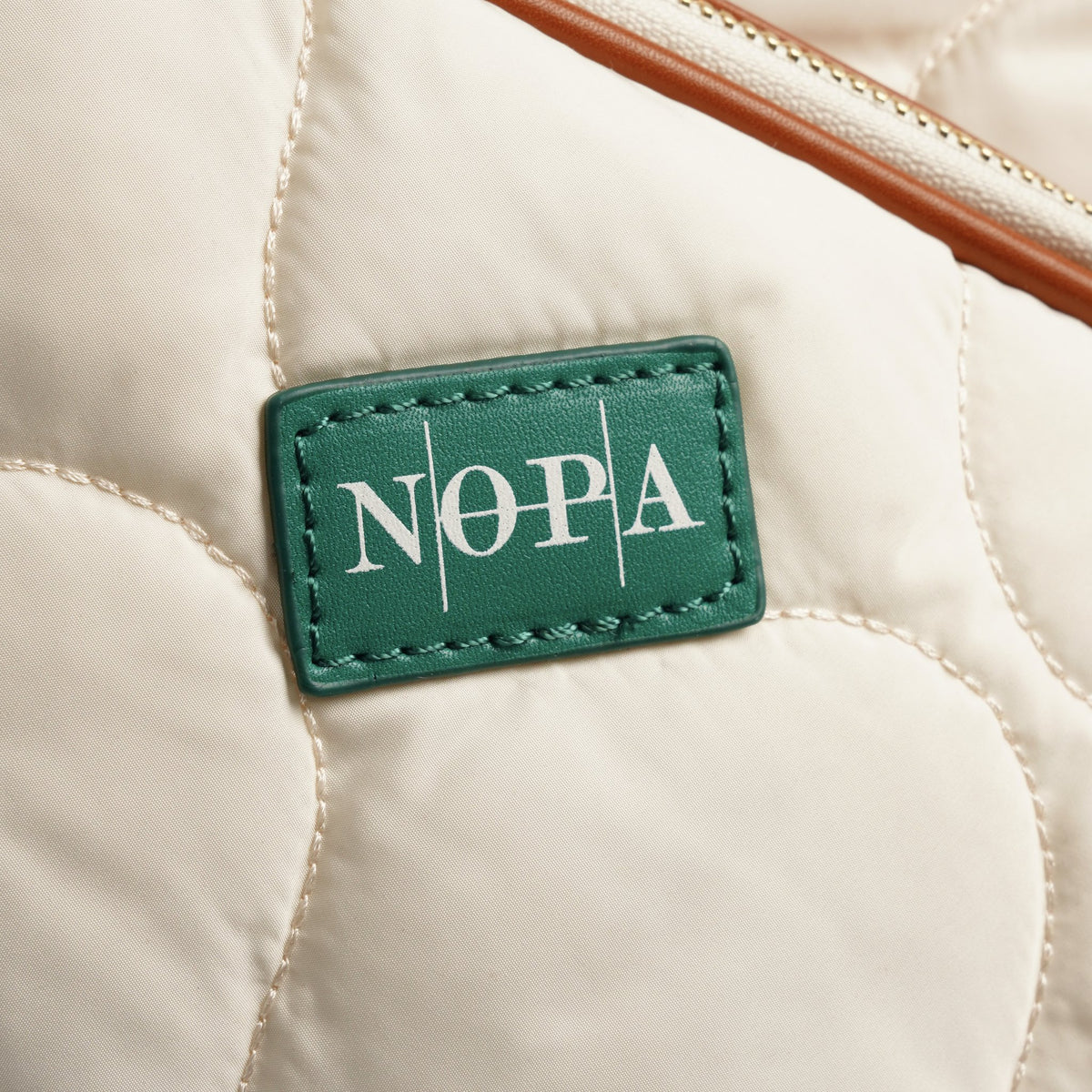Close-up of the green NOPA logo patch on the quilted padel tote backpack